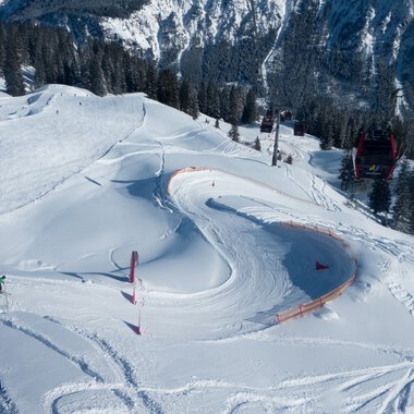 Snow-covered ski area with curves and avalanche barriers, surrounded by forest and mountains. | © Kleinwalsertal Tourismus eGen • Oberstdorf Kleinwalsertal Bergbahnen