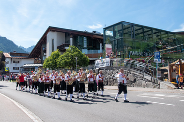 Musikkapelle beim Dorffest in Hirschegg marschiert an der Straße entlang bei sonnigem Wetter. | ©  Kleinwalsertal Tourismus eGen