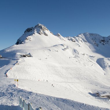 Snow-covered mountains in a ski resort with a blue sky, ski slopes, and lifts. | © Kleinwalsertal Tourismus eGen
