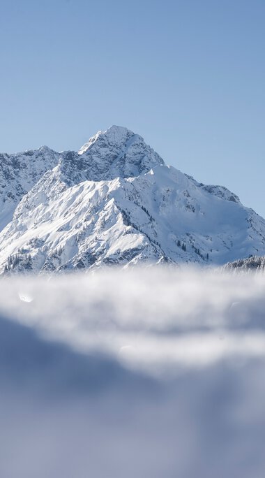 Snow-covered mountain landscape with peaks and blue sky, captured in a winter scene. | © Kleinwalsertal Tourismus eGen • Photographer: Dominik Berchtold