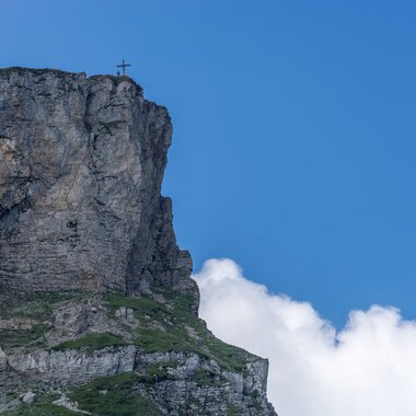 Felsen am Gipfel des Ifen mit Gipfelkreuz vor blauem Himmel und Wolken im Sommer. | © Kleinwalsertal Tourismus eGen • Fotograf: Steffen Berschin