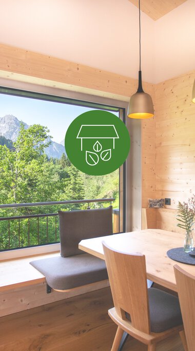 Gemütliches Raum mit großem Fenster, Blick auf grüne Berge, Holzmöbel und Hängelampen, ideal für nachhaltigen Genuss. | © Frank Drechsel • Haus Andrea