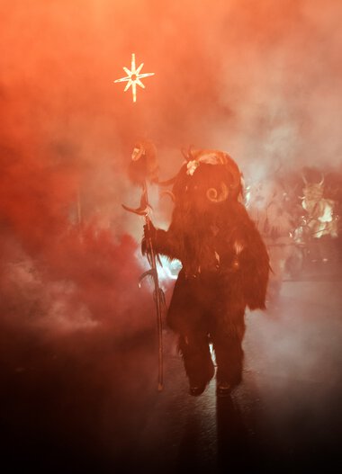 Krampus at the Advent magic, amidst smoke and fire, holding a star in hand during the Krampus hunt. | © Kleinwalsertal Tourismus eGen • Photographer: Dominik Berchtold