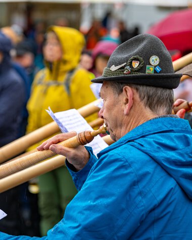 Musiker beim Alphornfestival 2024, der eine Notiz in der Hand hält und ein Alphorn spielt. | © Kleinwalsertal Tourismus eGen • Fotograf: Frank Drechsel